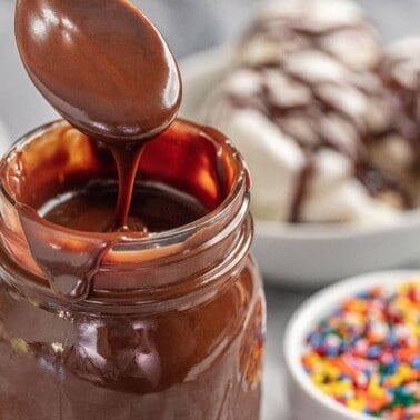 hot fudge sauce in a glass jar with a spoon dipping into it