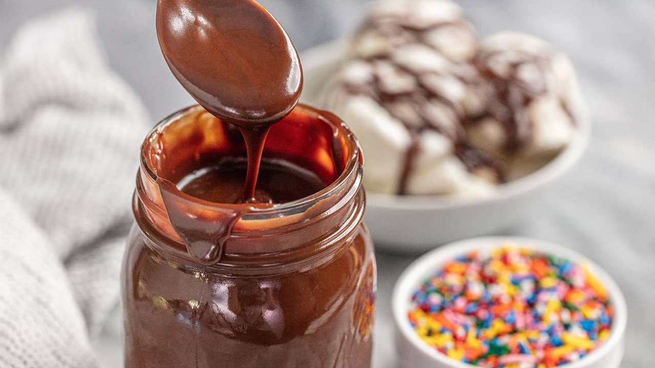 hot fudge sauce in a glass jar with a spoon dipping into it
