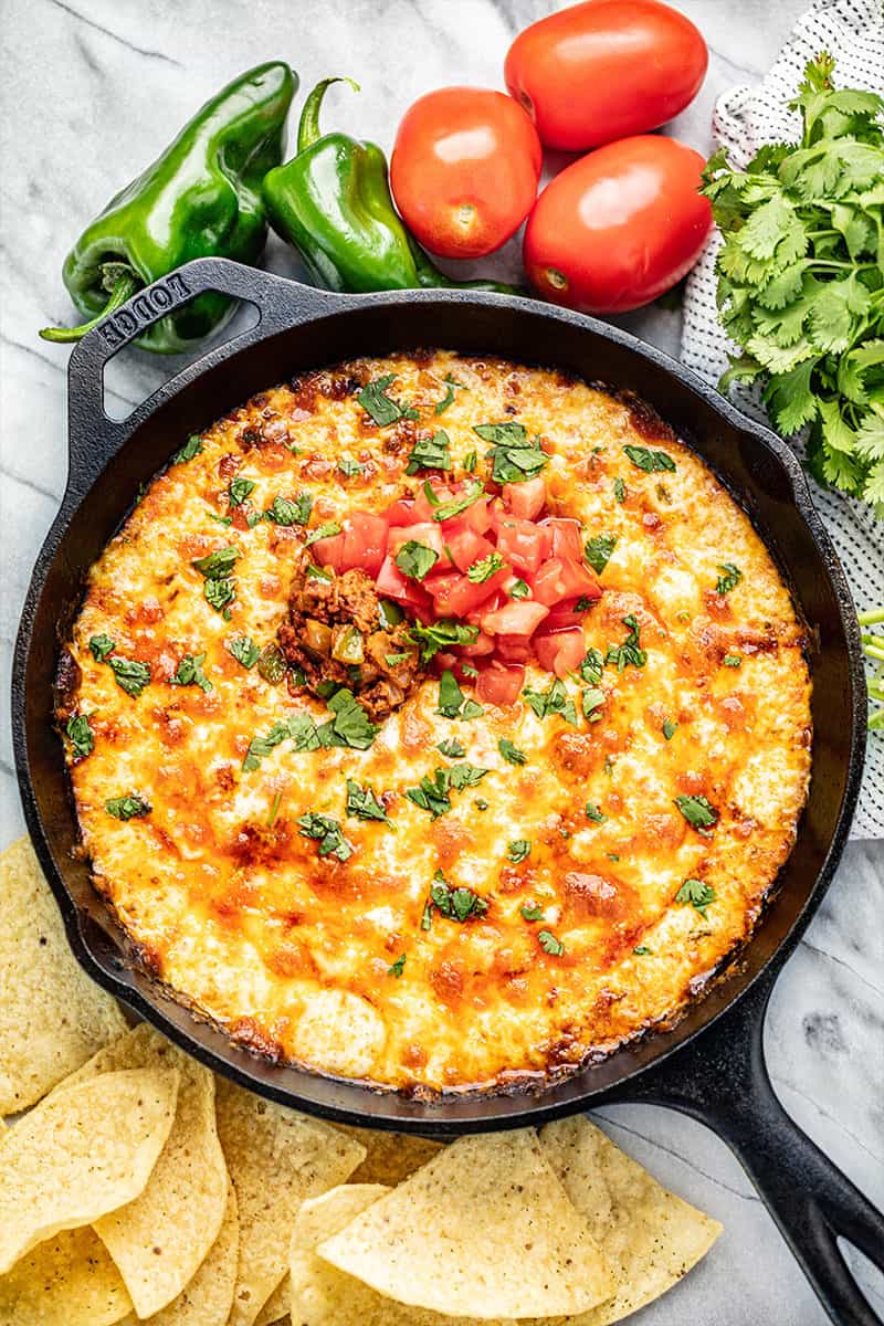 Queso Fundido in a skillet with bubbly cheese and topped with chorizo, fresh chopped tomato and cilantro