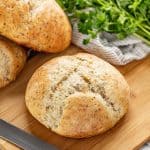 Hand holding a slice of rustic garlic parmesan herb bread with the rest of the loaf of bread in the background.