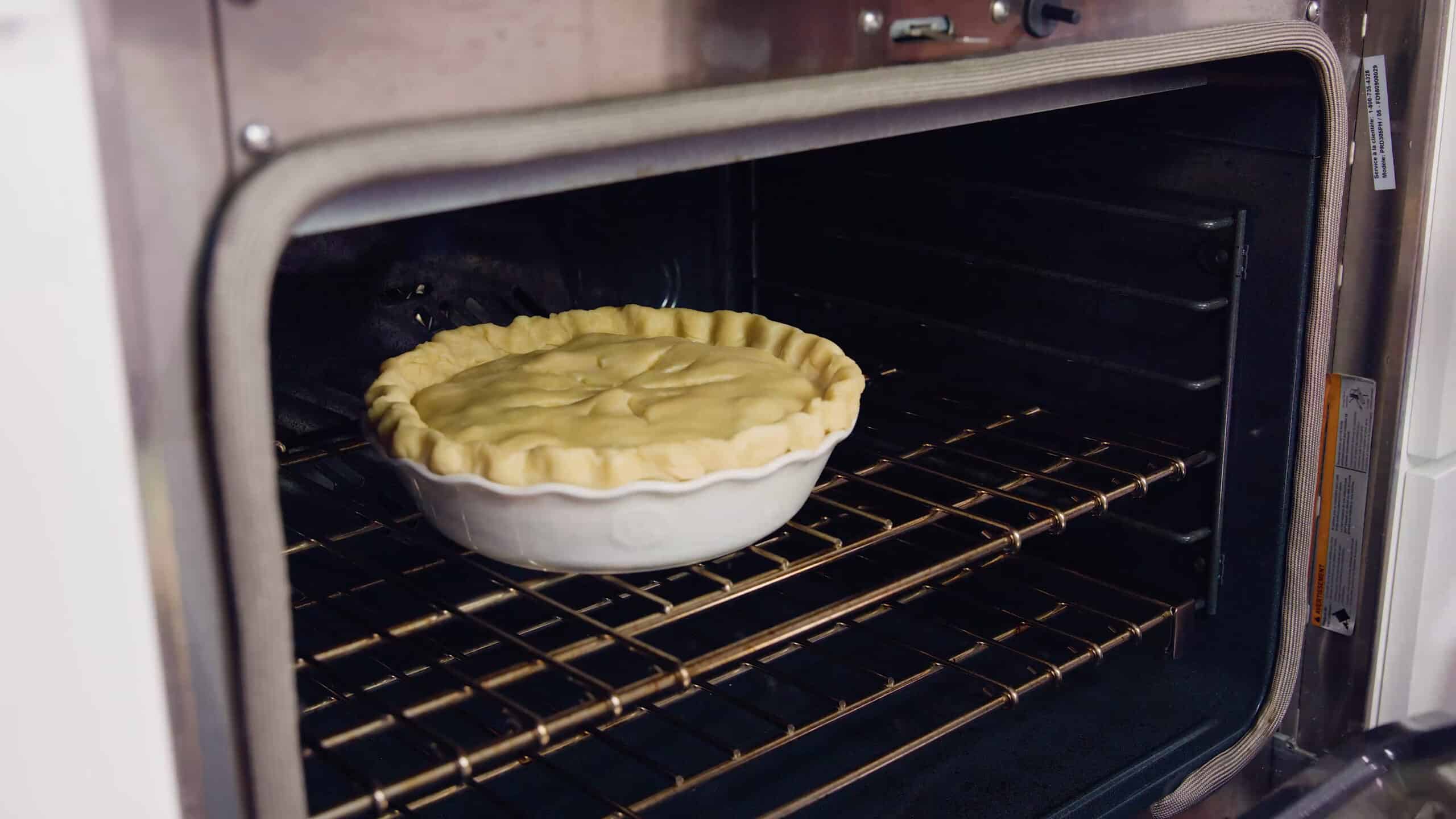 Angled view of open oven with fully prepared chicken pot pie on the rack in the middle of the oven.