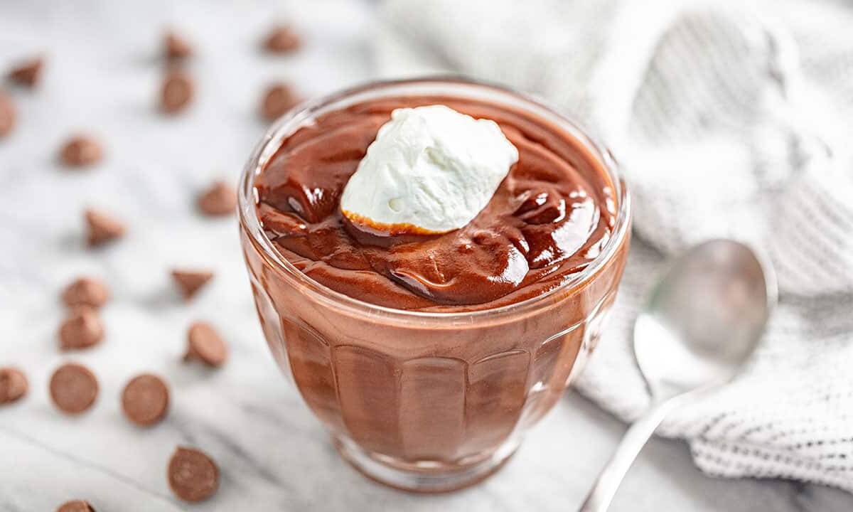 Angled view of Chocolate Pudding topped with whipped cream in a glass dish.