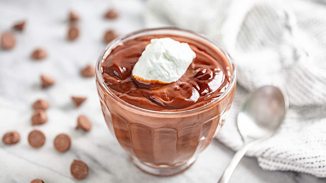 Angled view of Chocolate Pudding topped with whipped cream in a glass dish.