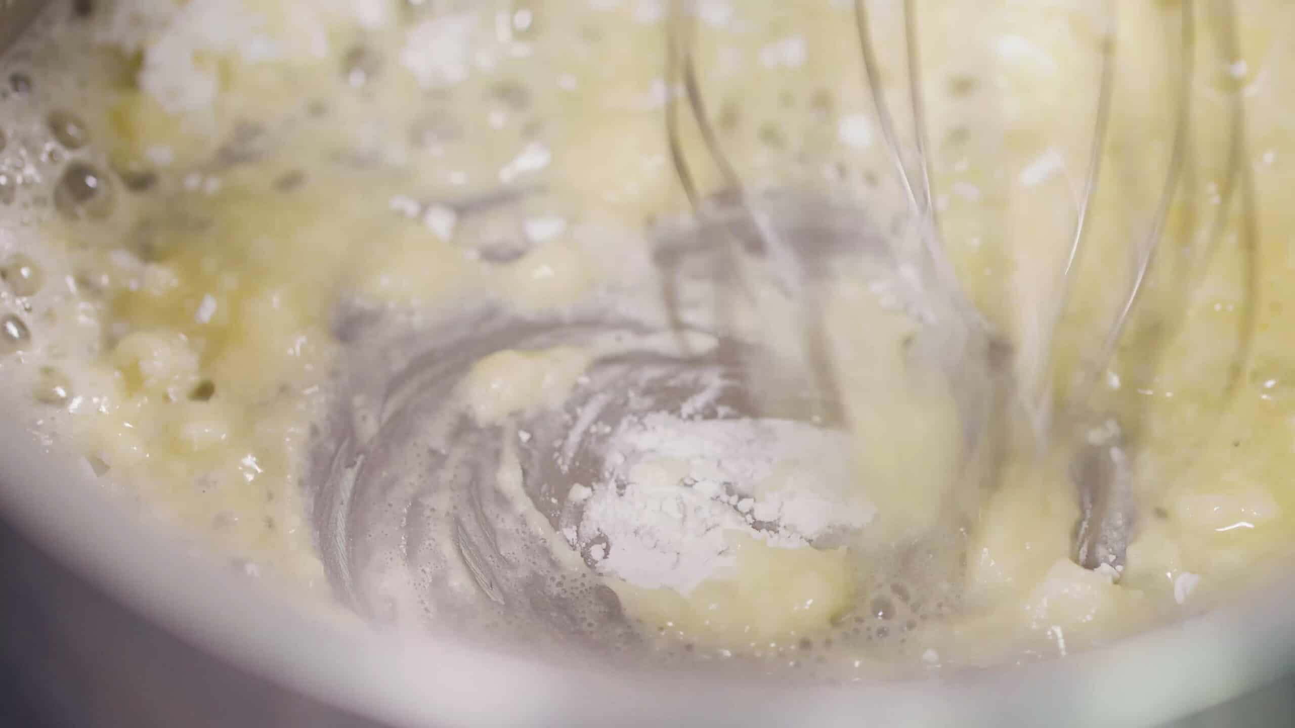 Close-up view of silver pot with melted butter and cornstarch with a wire whisk used to combine.