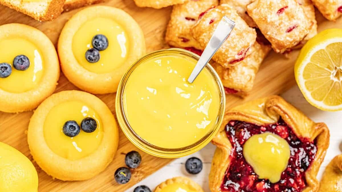 Bird's eye view of Lemon curd in a glass bowl with a spoon in it surrounded by various pastries.