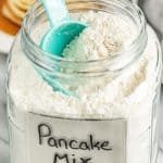 A glass container full of Pancake Mix with a measuring cup in it.