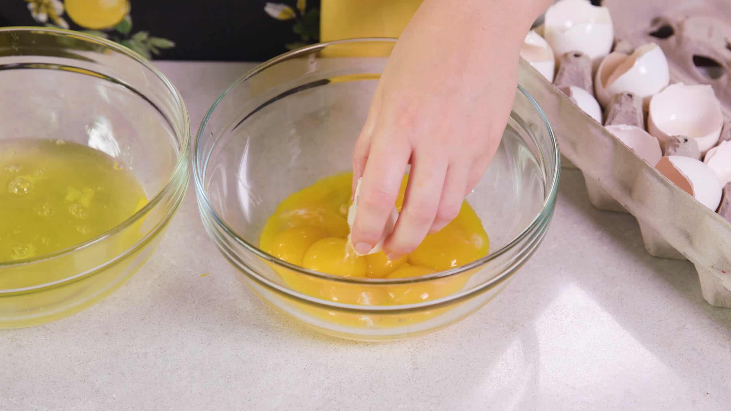 Angled view of medium sized mixing bowl with egg yolks on a marble countertop and another mixing bowl to the side with egg whites.