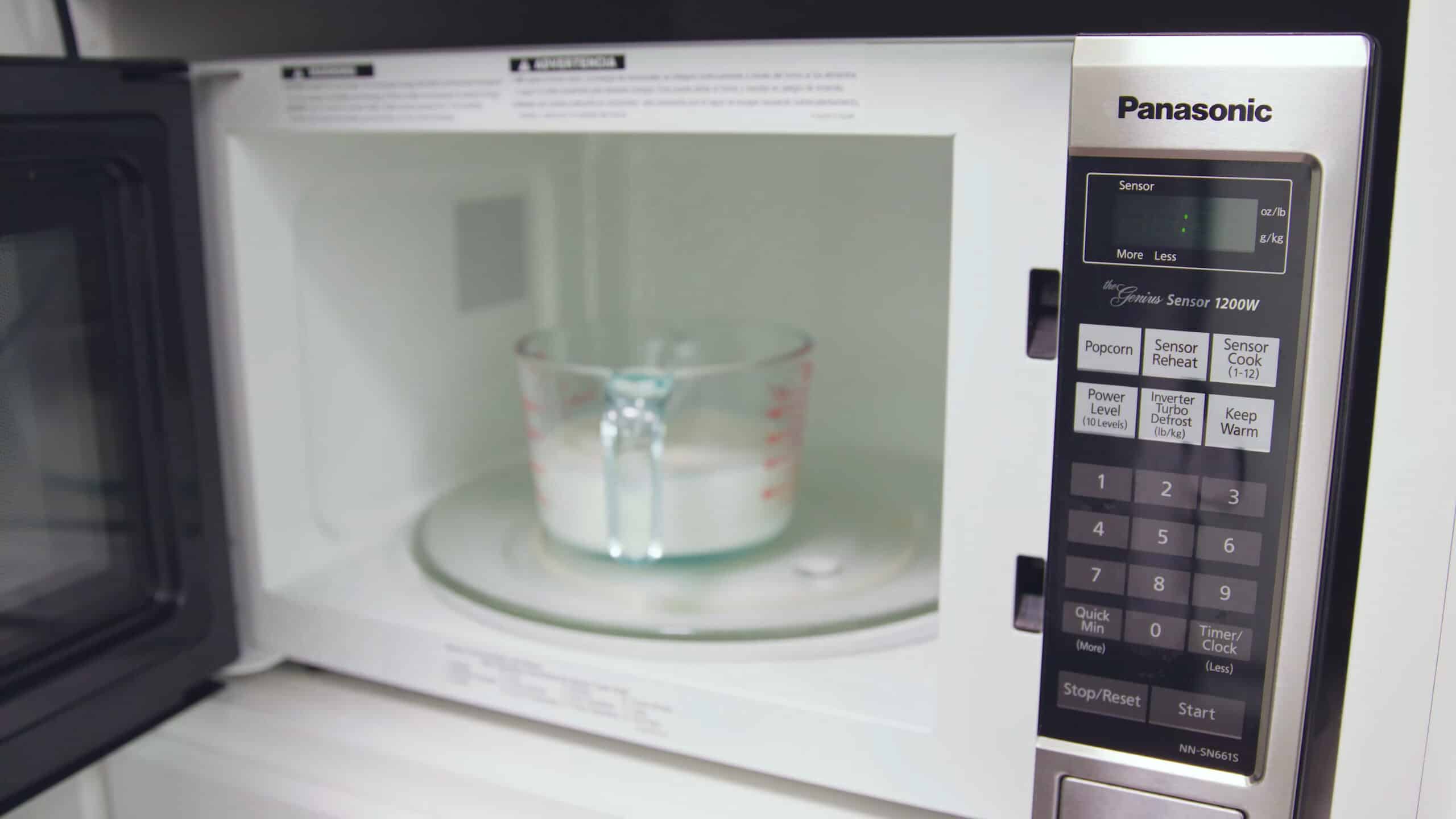 Angled view of clear glass measuring cup with milk inside microwave ready for heating.