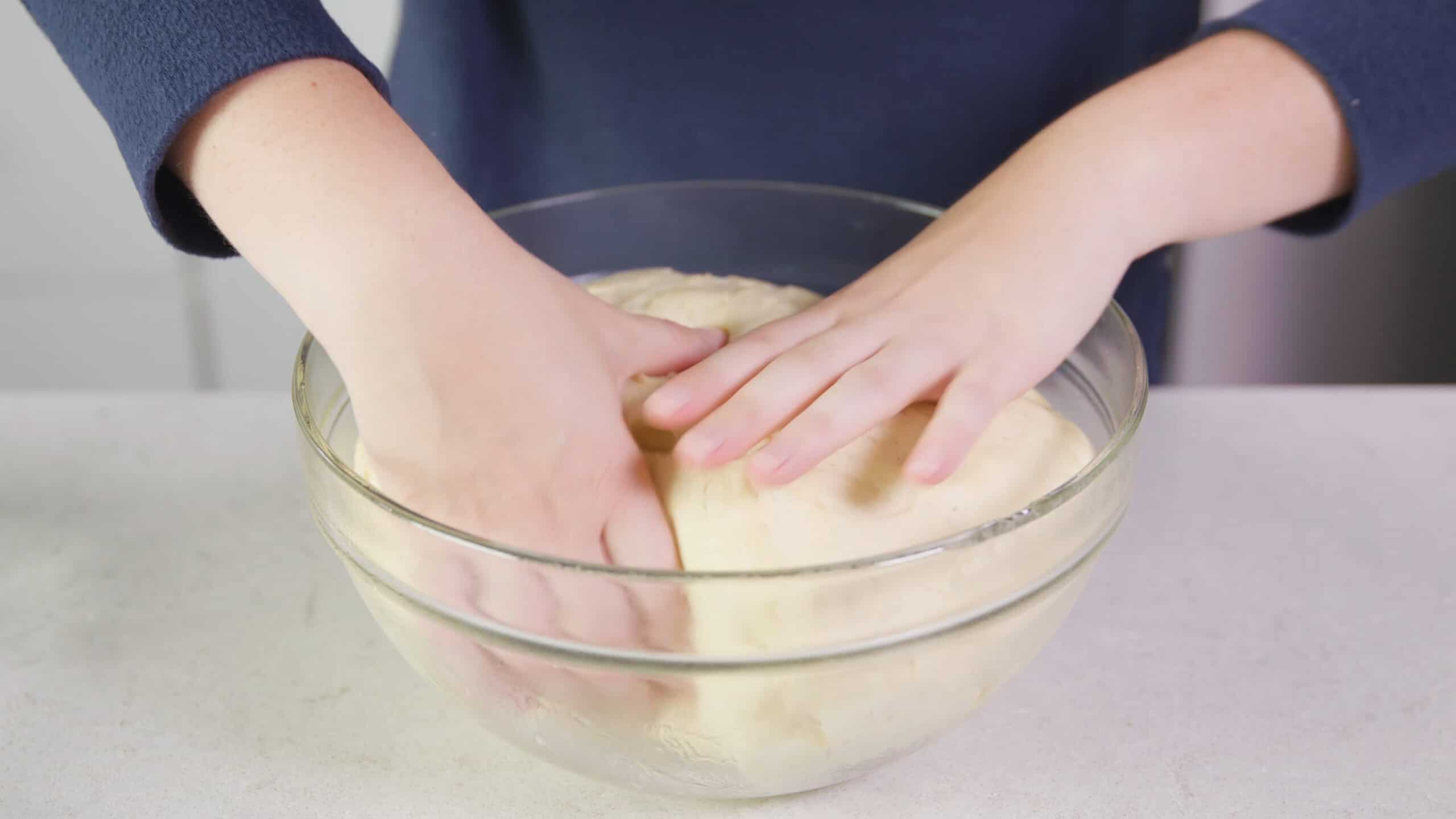 Angled view of risen dough in large clear glass mixing bowl being split into two equal portions.