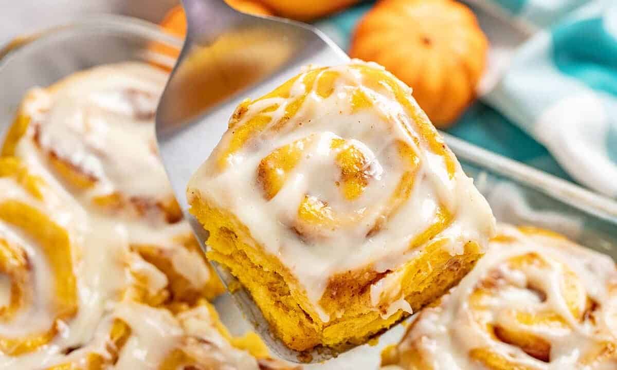Pumpkin Cinnamon Roll being held up with a metal spatula.