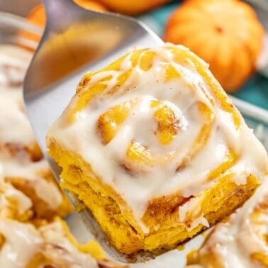 Pumpkin Cinnamon Roll being held up with a metal spatula.