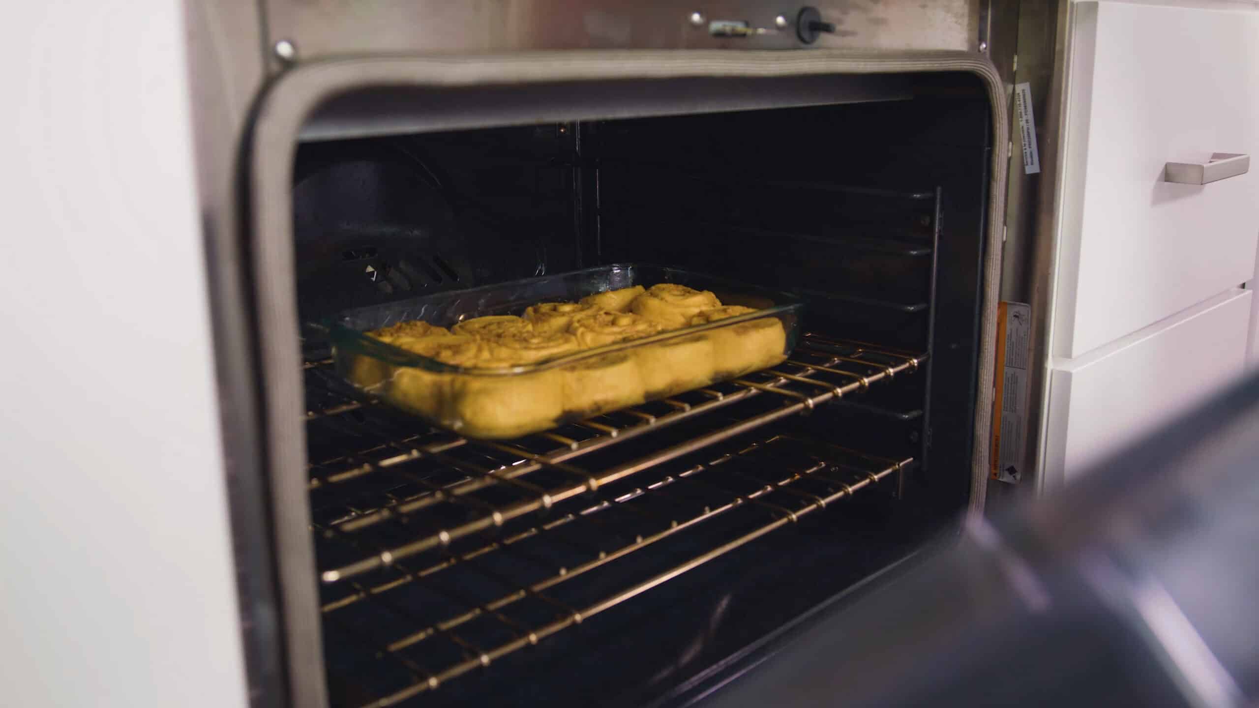 Angled view of open oven with a clear glass baking dish filled with one dozen pumpkin cinnamon rolls ready for baking on the rack in the middle of the oven.