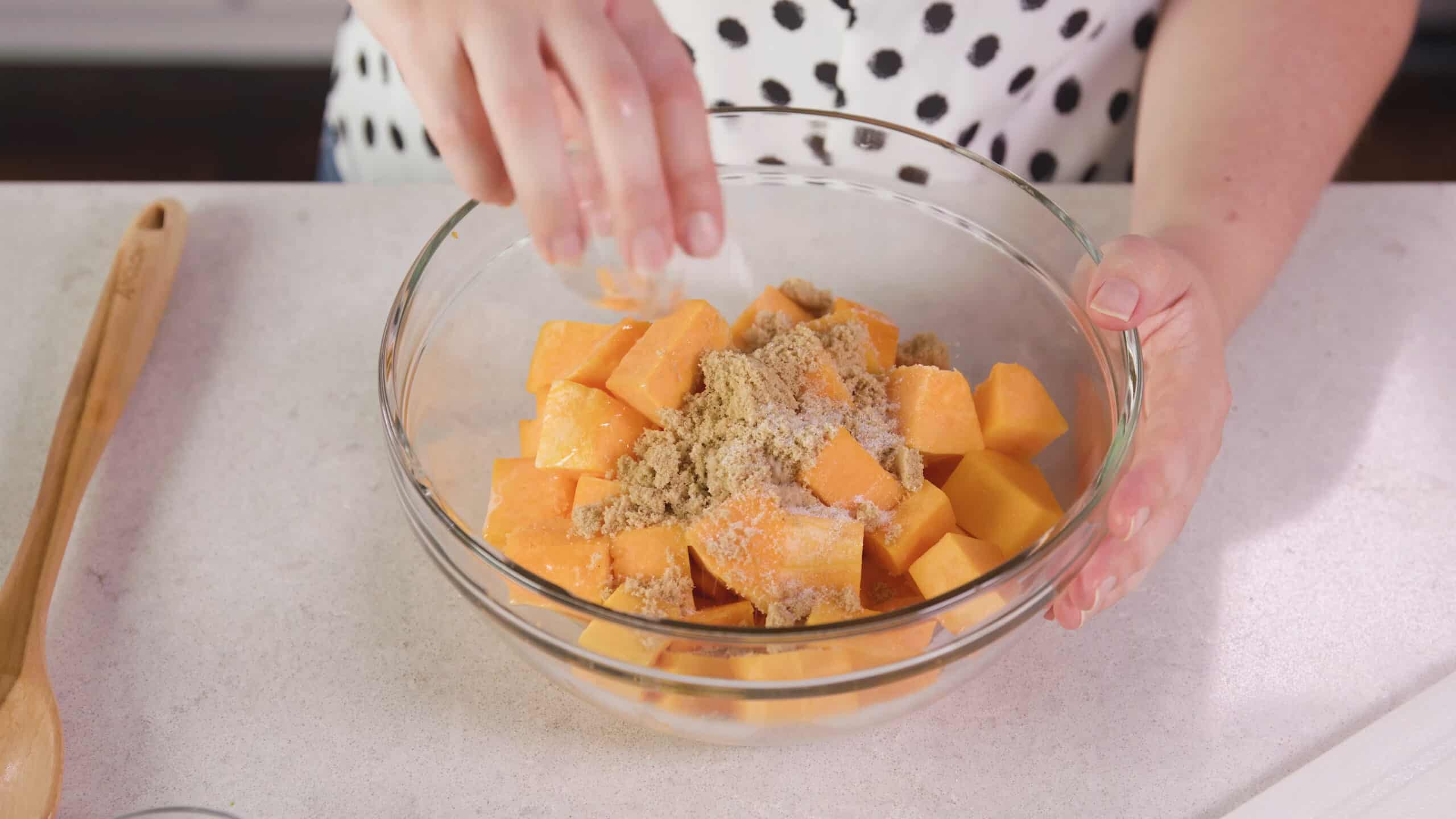 Angled view of large sized mixing bowl with diced butternut squash flavored with brown sugar and salt.