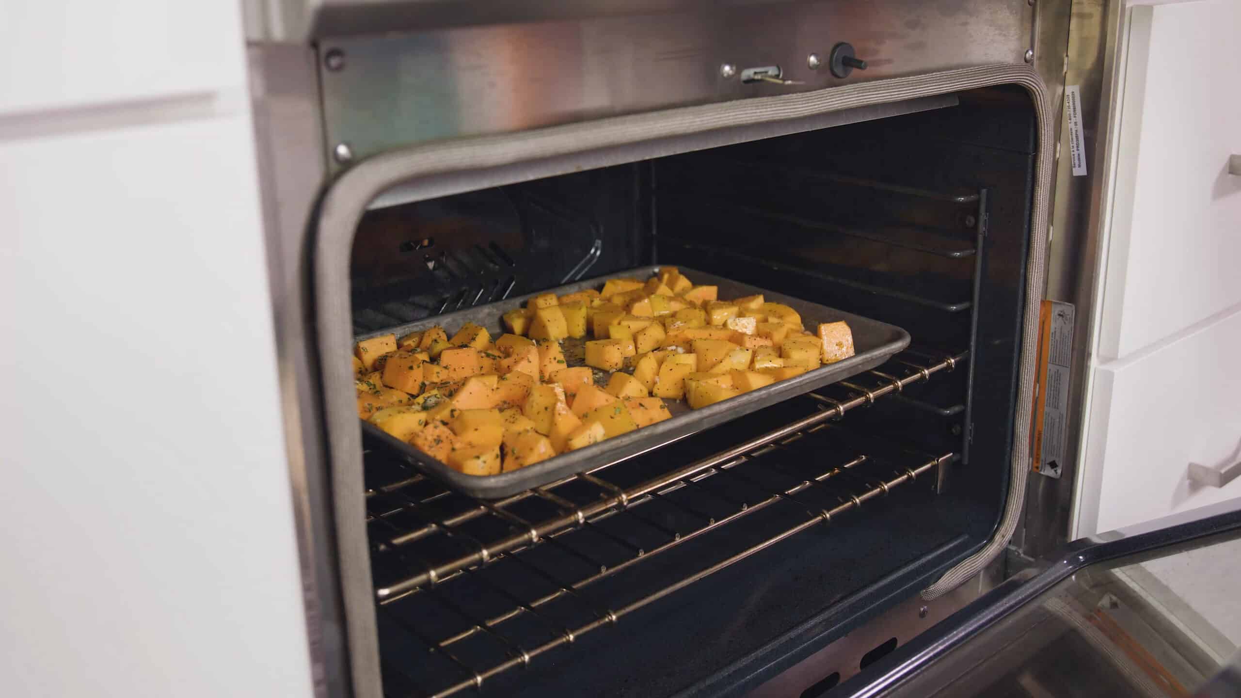 Angled view of open oven with a silver baking sheet with savory flavored butternut squash placed on each in the middle of the oven.