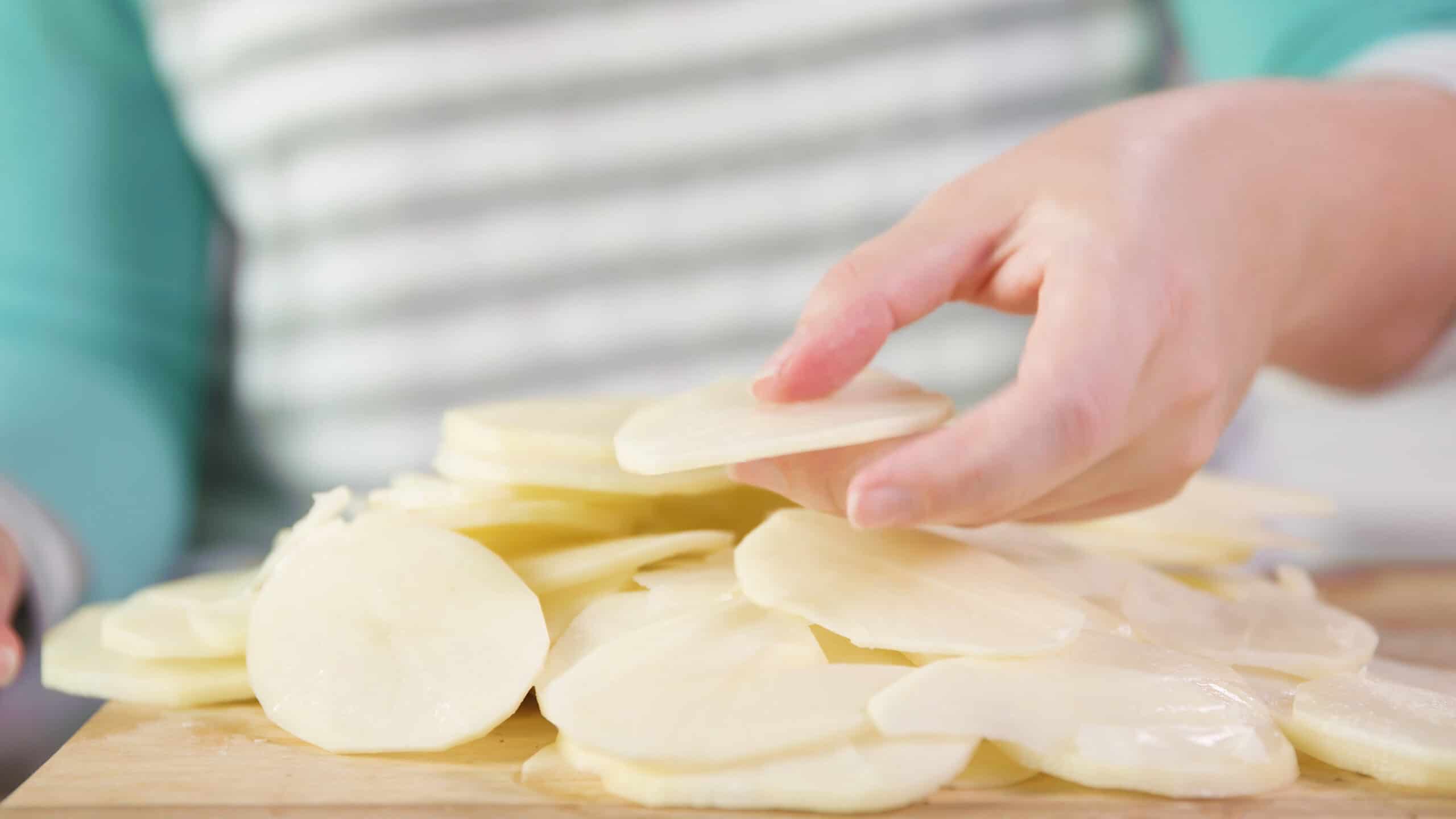 Close-up view of thinly sliced and peeled russet potatoes on cutting board.