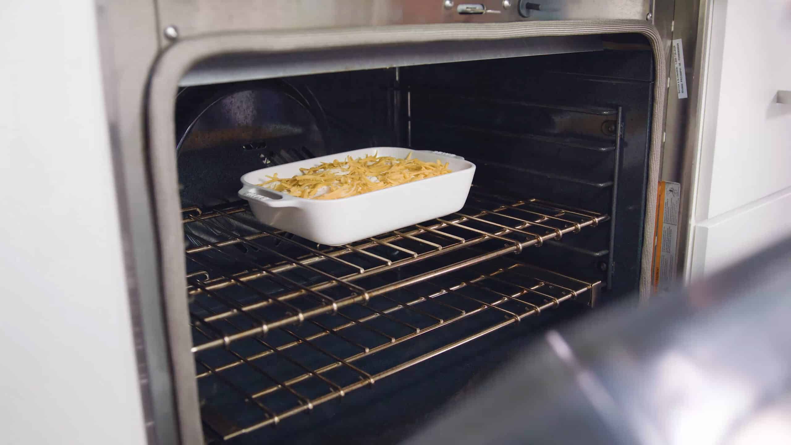Angled view of open oven with white casserole dish filled with cheesy scalloped potatoes on a rack in the middle of the oven.