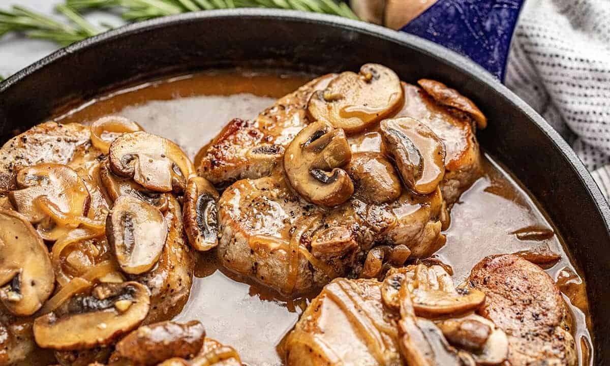 Smothered Pork Chops covered in mushrooms in a cast-iron skillet.