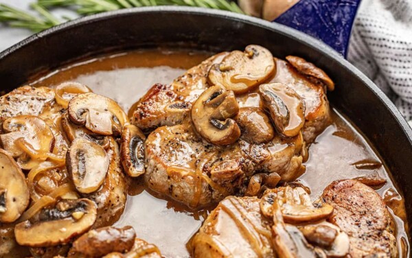 Smothered Pork Chops covered in mushrooms in a cast-iron skillet.