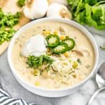 White Chicken Chili topped with cheese jalapeno slices and sourcream all in a white bowl.