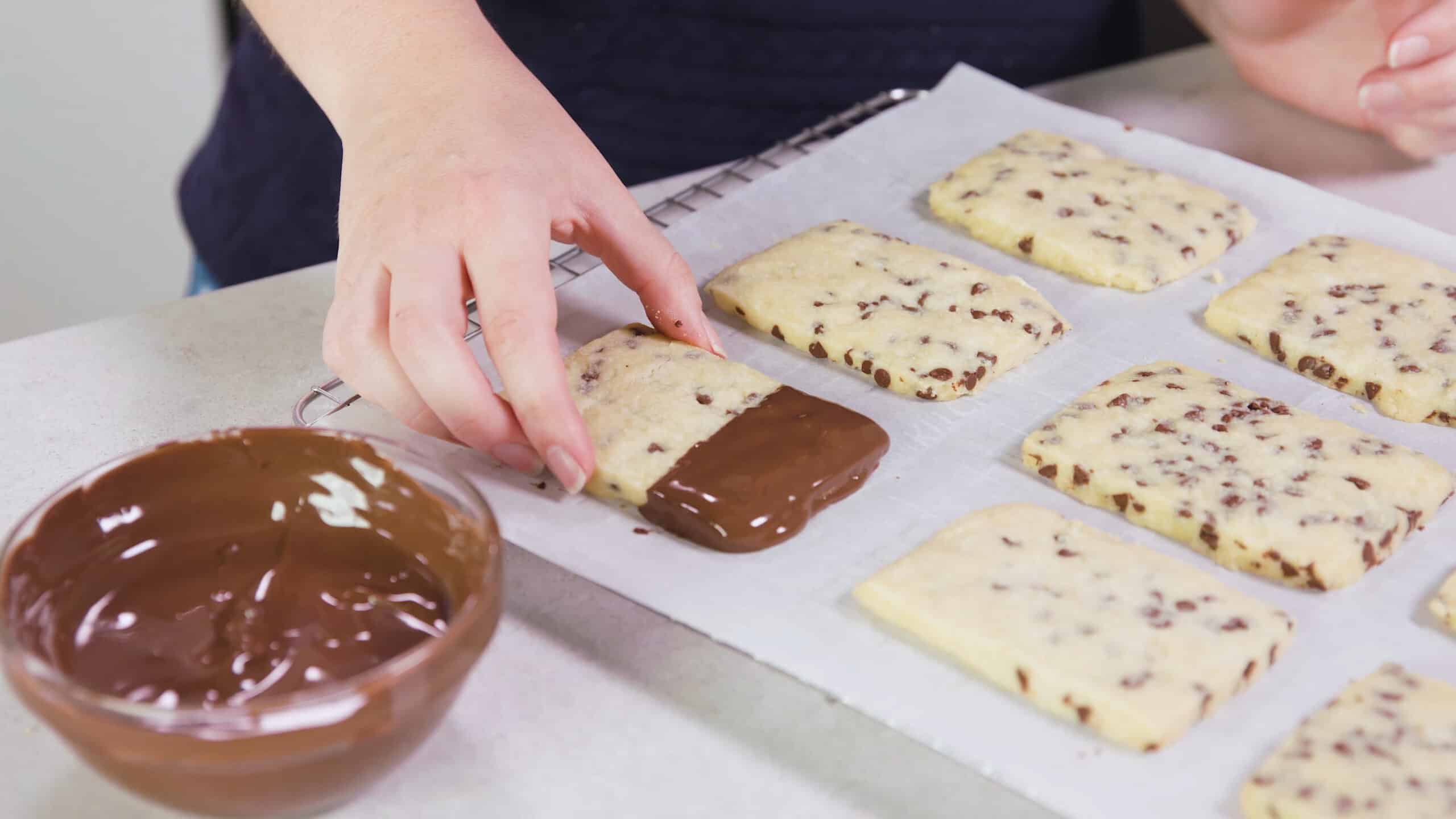 Angled view of a cooling rack lined with parchment paper and filled with chocolate chip shortbread cookies one that has been dipped in melted chocolate on the end.