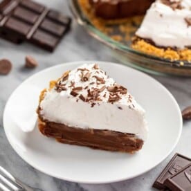 Slice of chocolate cream pie on a plate with the whole pie in the background