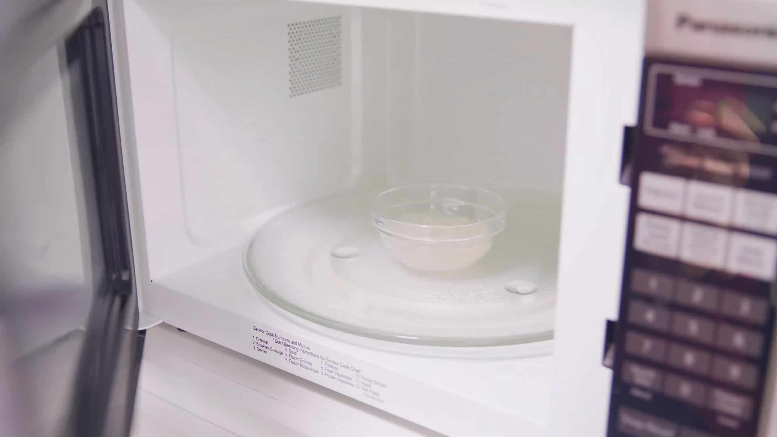 Angled view of open microwave with view of small glass bowl filled with gelatin that is intended to add to the whipped cream topping.