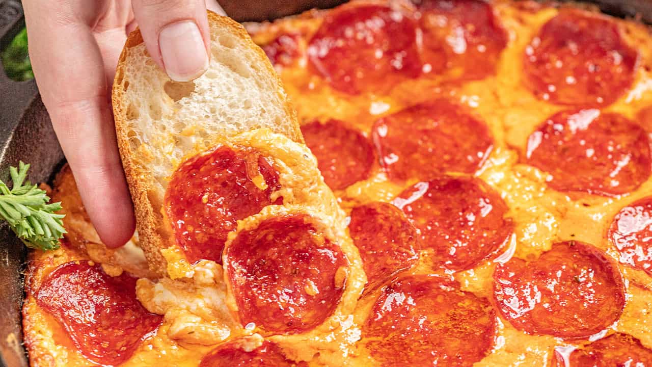 Hand dipping french bread into pizza dip with pepperoni