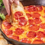 Hand dipping bread into pizza dip in a skillet