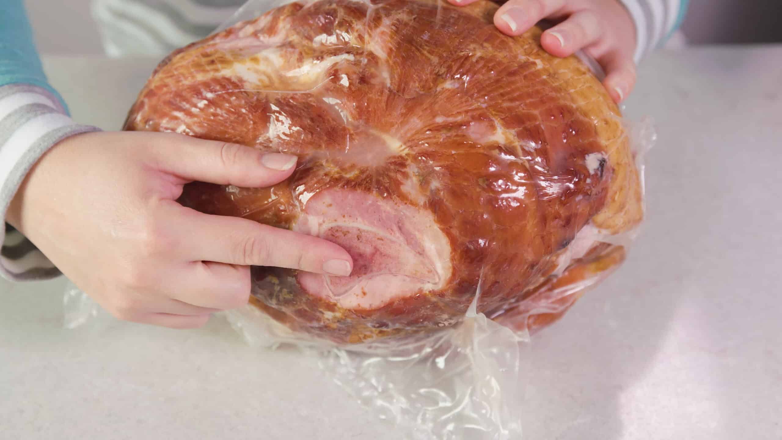 Close-up view of the side of vacuum plastic sealed ham and pointing out the "bone-in" portion of this particular cut of meat.