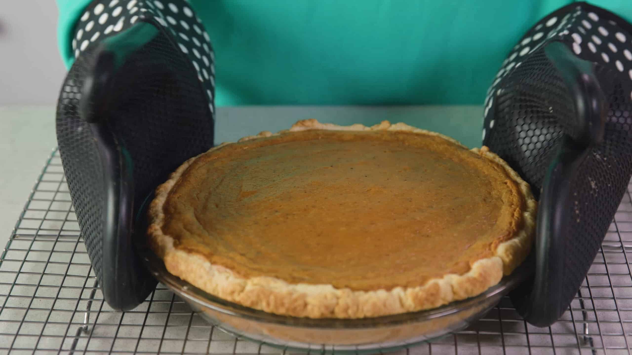 Angled view of clear glass pie plate with fully cooked sweet potato pie resting on cooling rack while on a marble countertop.