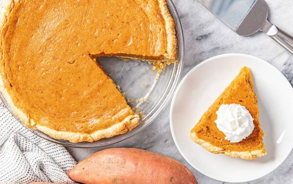 Bird's eye view of full Sweet Potato Pie with a single slice cut out and placed on a white plate topped with whipped cream.