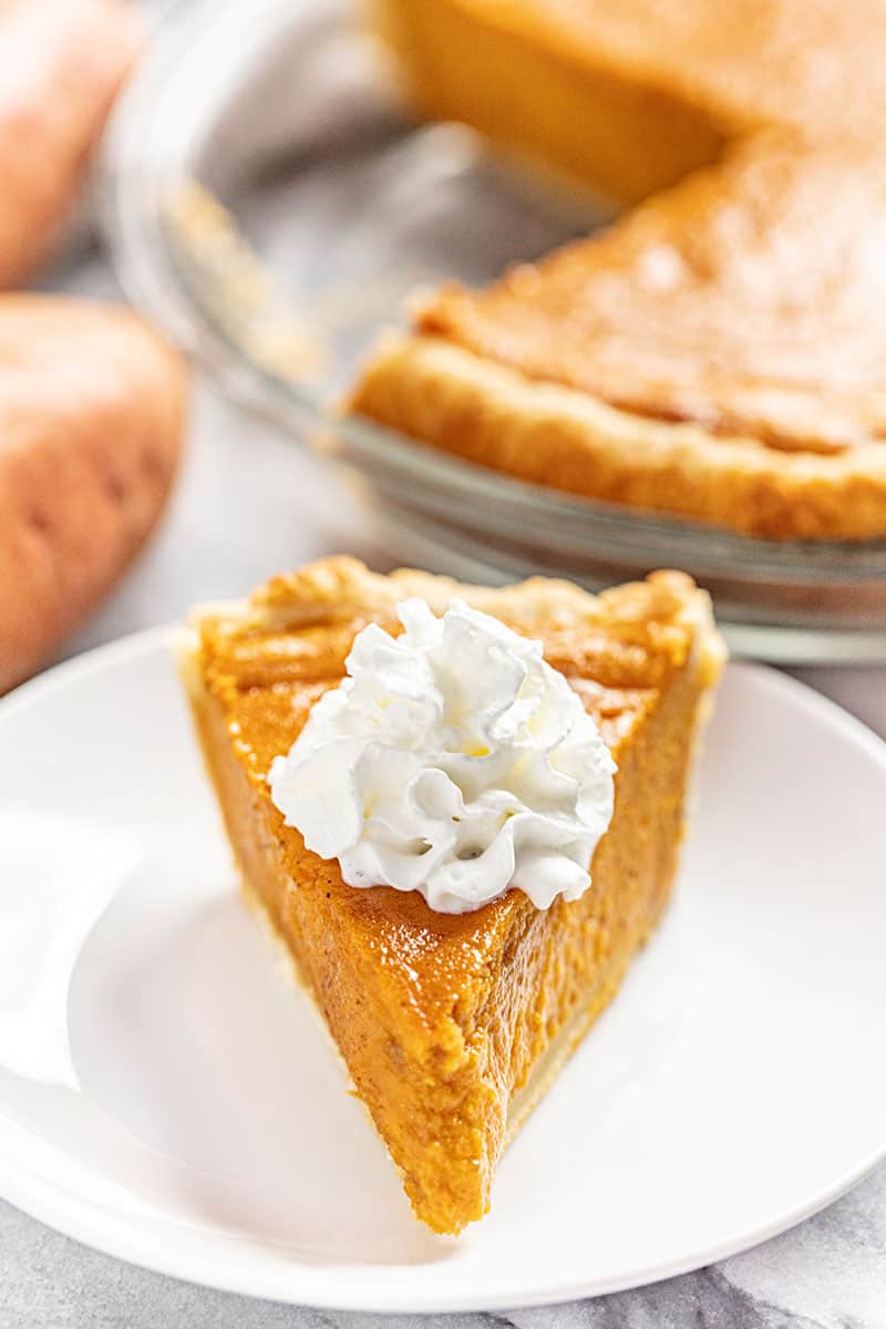 Slice of Sweet Potato Pie topped with whipped cream on a white plate.
