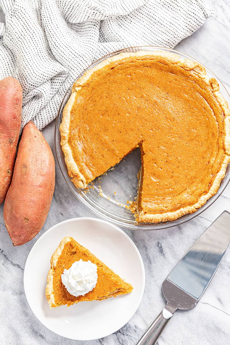 Bird's eye view of Sweet Potato Pie with a slice out of it and a slice of potato pie topped with whipped cream on a white plate.