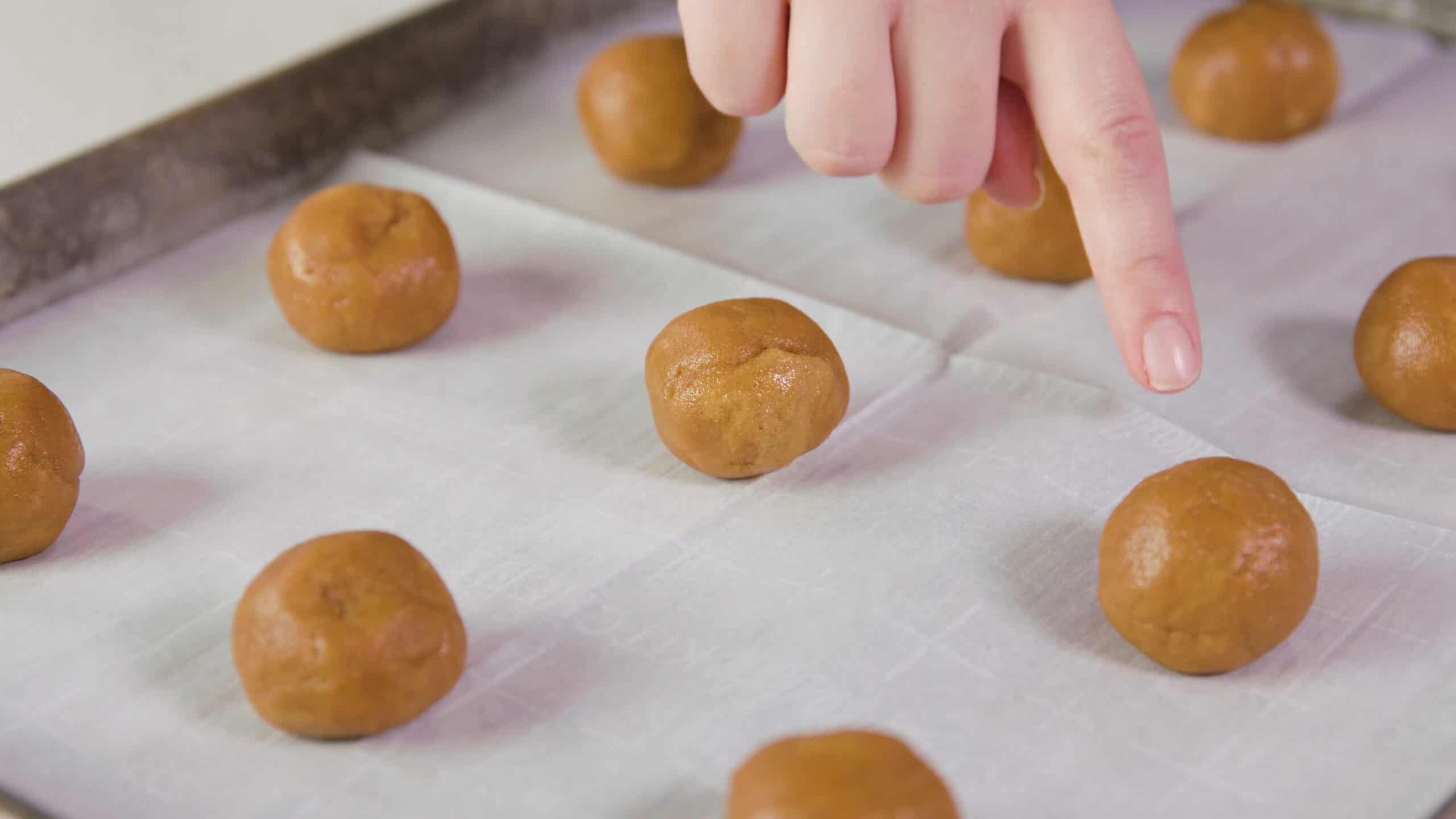 Close-up view of silver baking sheet lined with parchment paper and peanut butter cookie dough balls on top.