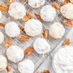 Pecan Sandies on a wire cooling rack with pecans and a bowl of powdered sugar