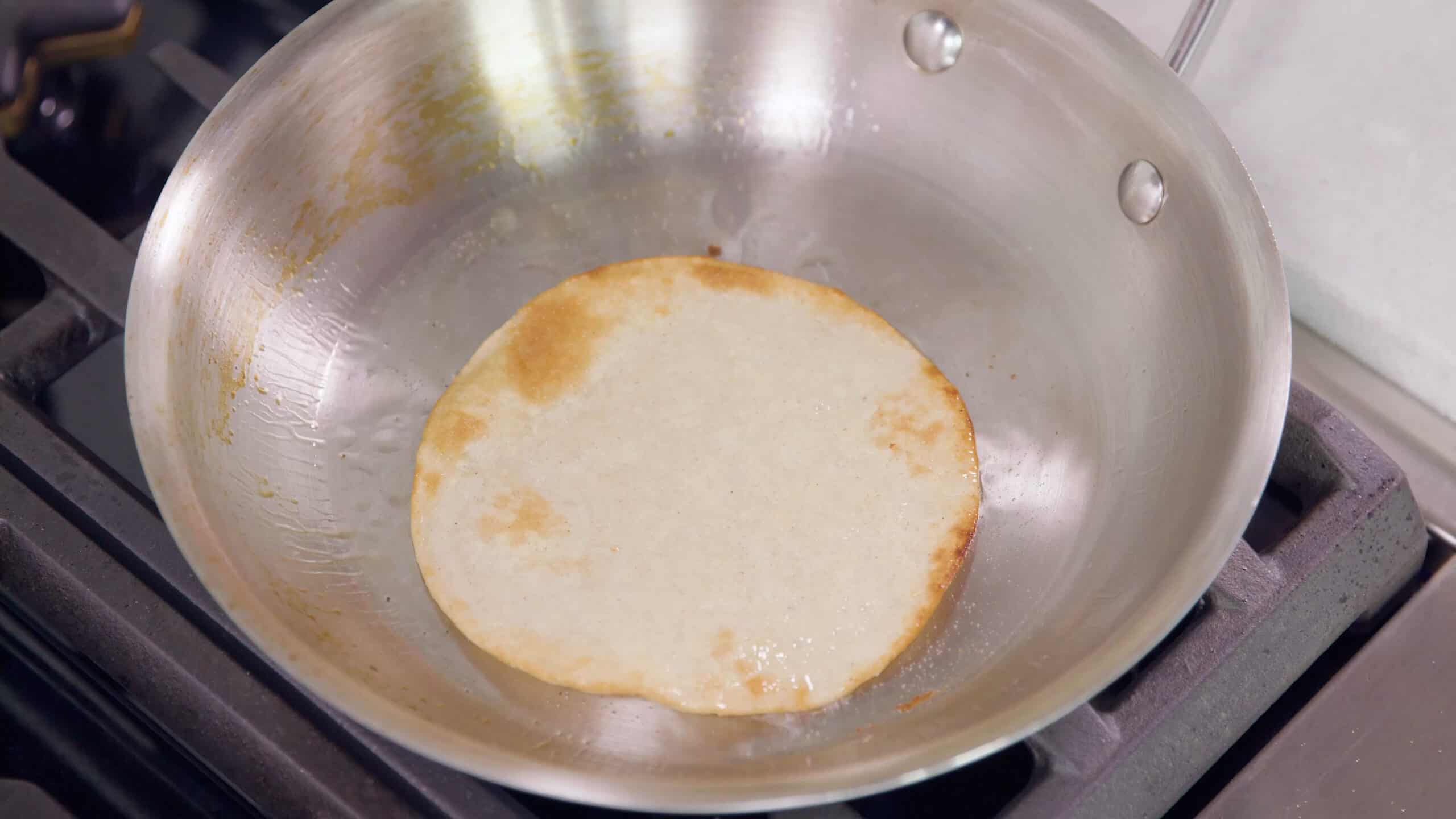 Overhead view of metal saucepan with piping hot oil and a single tortilla frying in the pan.