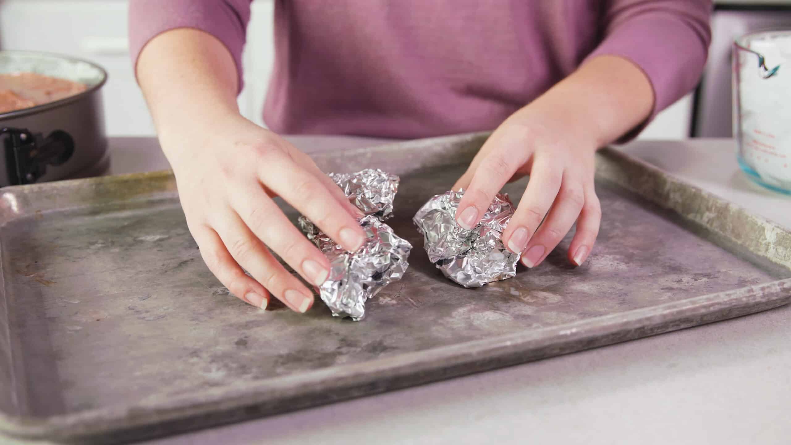 Angled view of a metal baking sheet with three balls of aluminum foil that will form a triangular stand for the spring form pan to rest on.