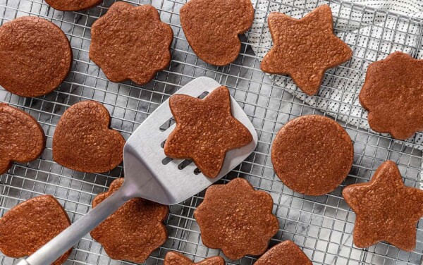 Bird's eye view of freshly baked chocolate sugar cookies laid on a wire cooling rack with a silver spatula picking up one star shaped cookie.