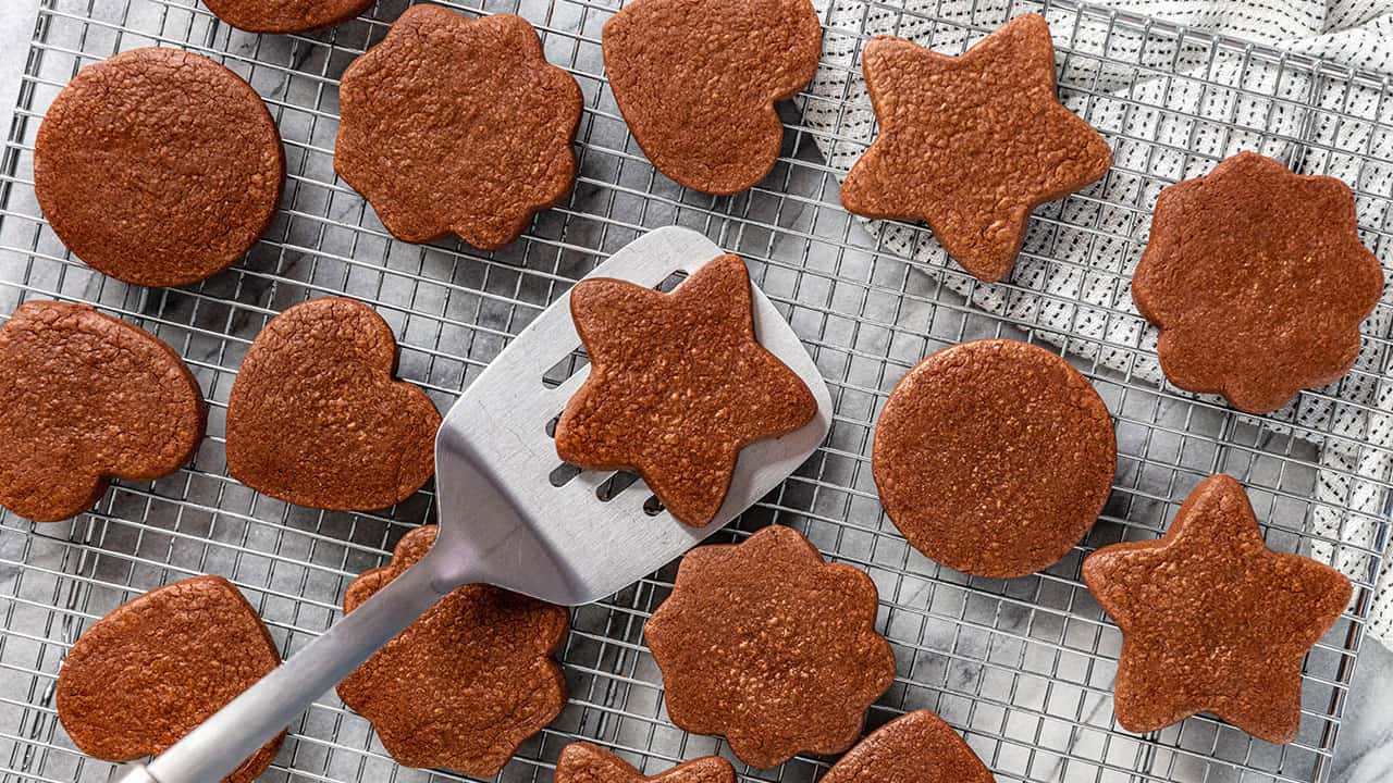 Bird's eye view of freshly baked chocolate sugar cookies laid on a wire cooling rack with a silver spatula picking up one star shaped cookie.