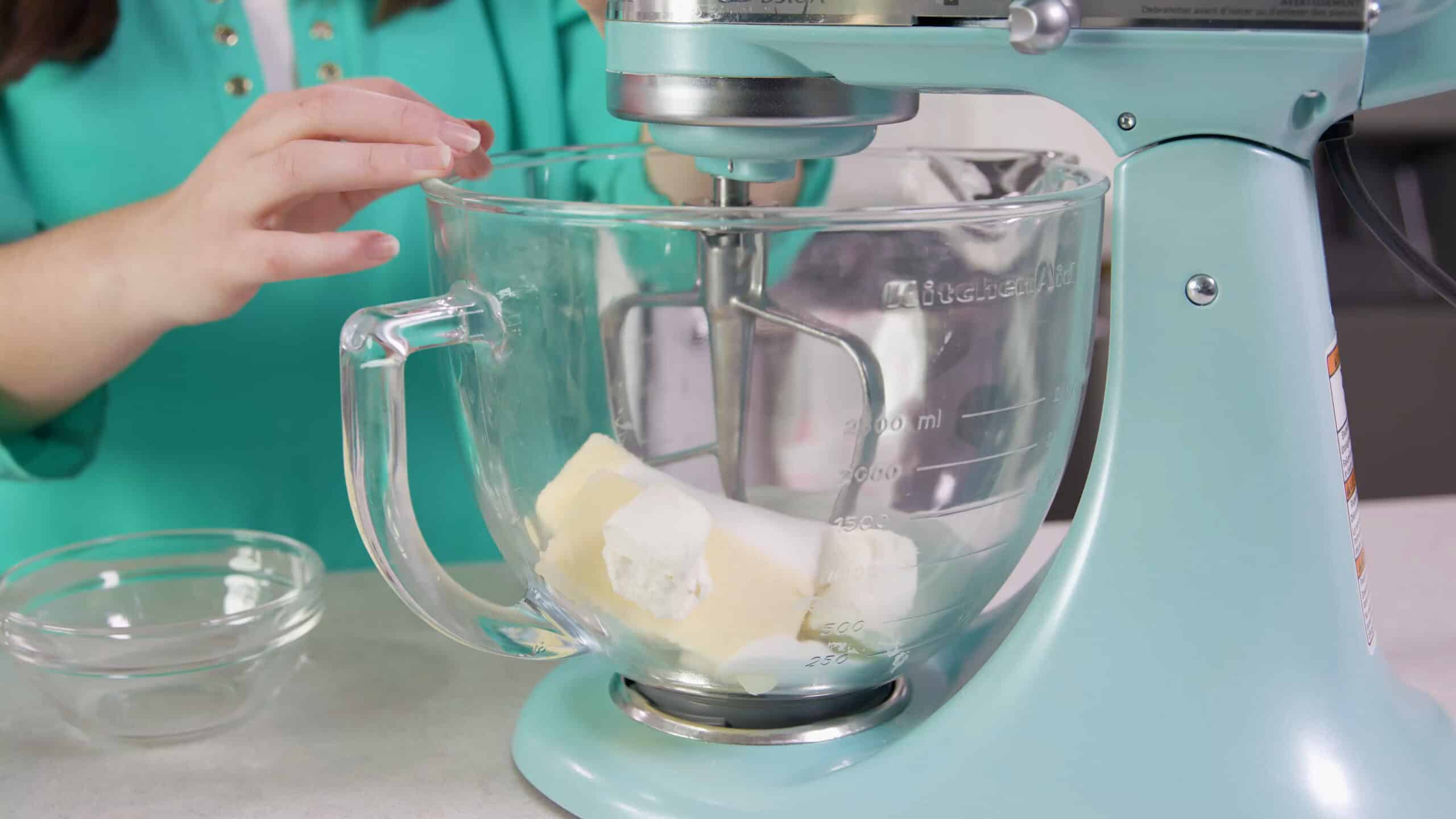 Side view of large measuring cup connected to a countertop stand mixer filled with butter, granulated sugar, and cream cheese.