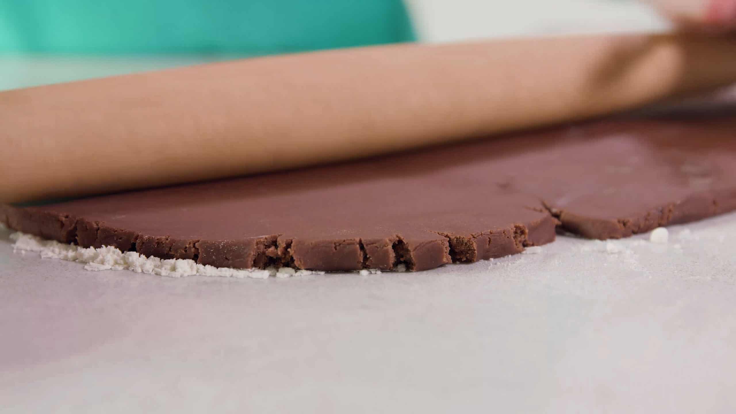 Side view of rolled chilled chocolate sugar cookie batter with a rollin pin setting the width to 1/4 inch thickness all on a clean floured marble countertop.