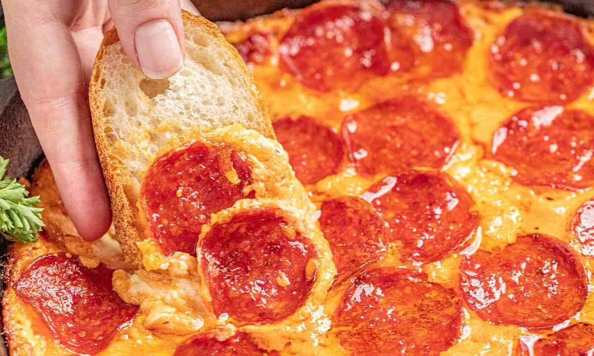 Hand dipping bread into pizza dip in a skillet