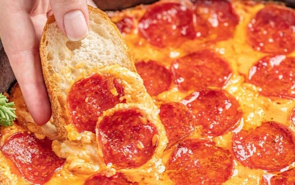 Hand dipping bread into pizza dip in a skillet