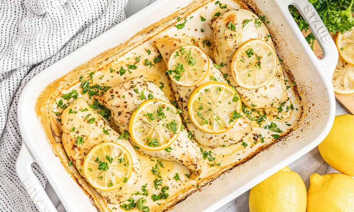 Bird's eye view of Lemon Herb Baked Chicken Breasts in a white baking dish topped with lemon slices and chopped parsley.