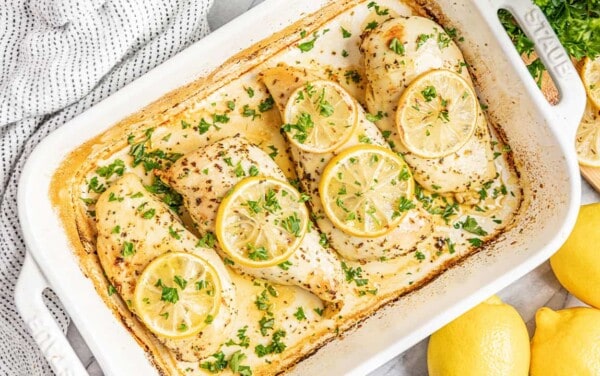 Bird's eye view of Lemon Herb Baked Chicken Breasts in a white baking dish topped with lemon slices and chopped parsley.
