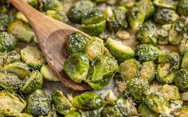 A wooden spoon scoops up Garlic Butter Roasted Brussel Sprouts from a sheet pan.