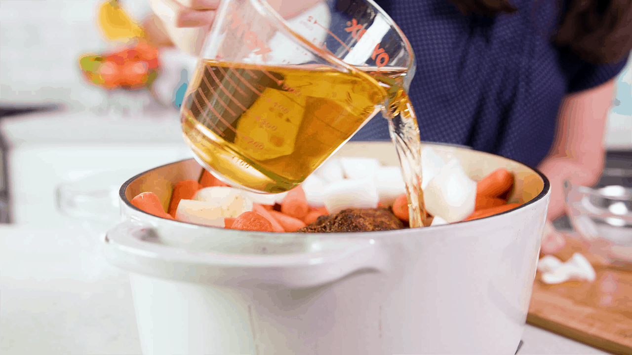 Apple juice being poured over a pork roast and vegeatbles