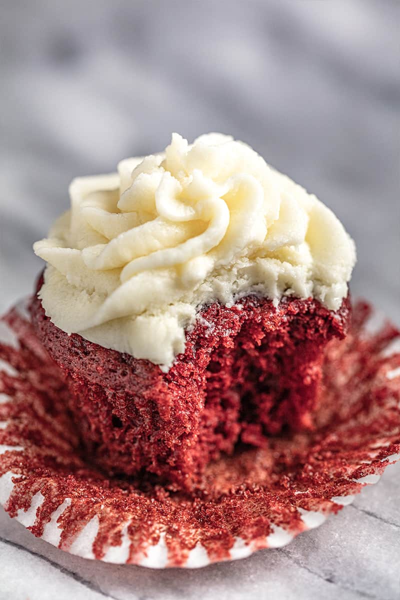 Red velvet cupcake with ermine frosting with a bite taken out of it