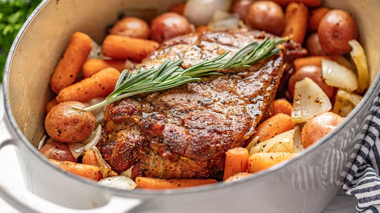 Pork Roast surrounded by carrots, potatoes, and onion in a cast iron dutch oven