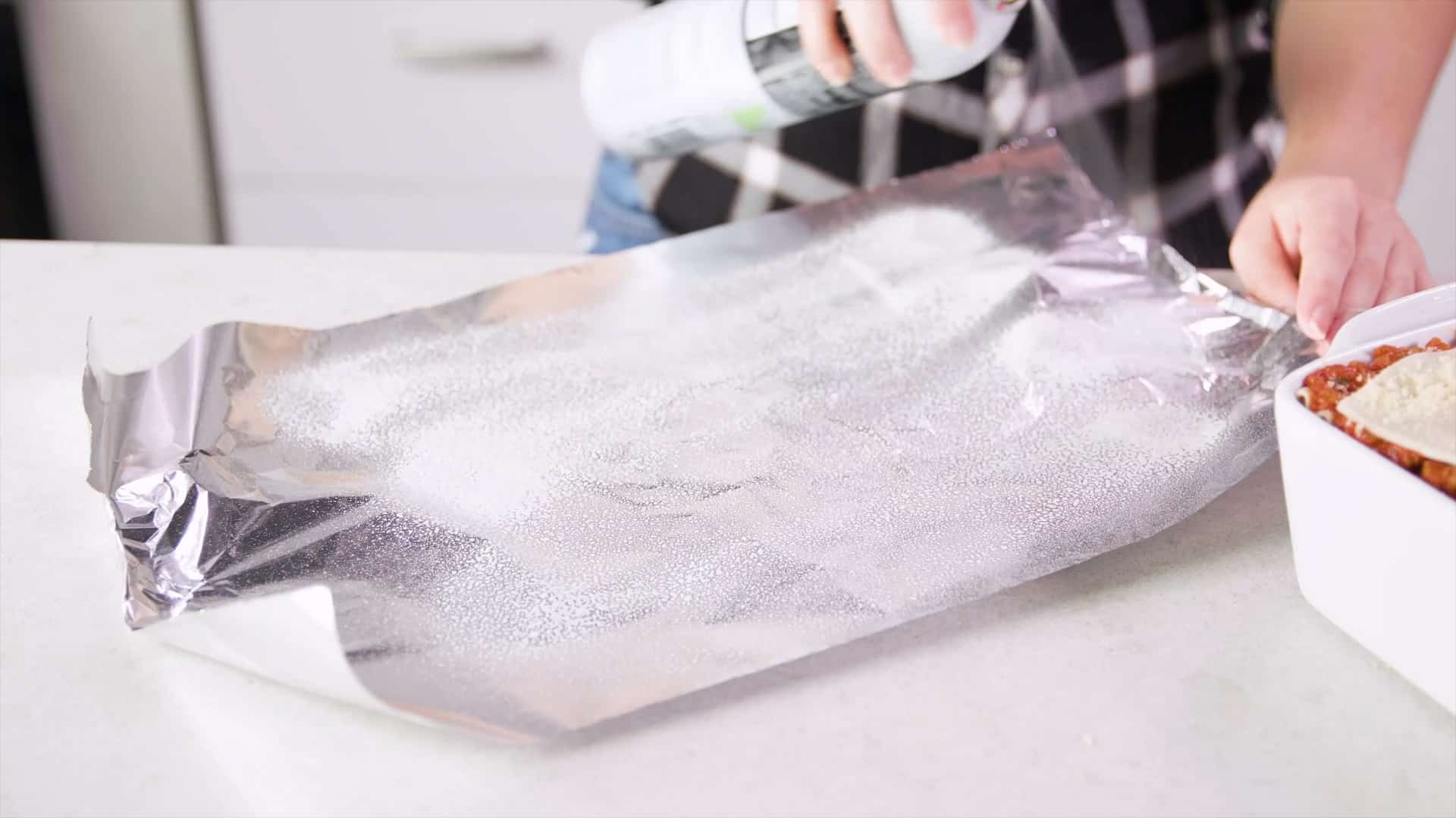 Angled view of a long sheet of aluminum foil shiny side up being sprayed with oil.